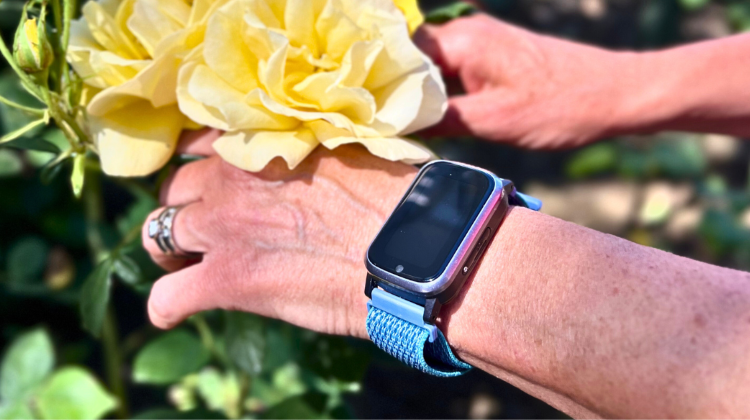 Kvinnohand med trygghetslarm från Sensorem plockar gul blomma.