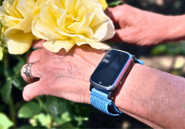 Kvinnohand med trygghetslarm från Sensorem plockar gul blomma.